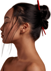 Profile of a woman with her eyes closed peacefully, and her hair up in a bun with chop sticks.